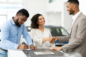 Couple Shaking Hands With Salesman In Cars Selling Center